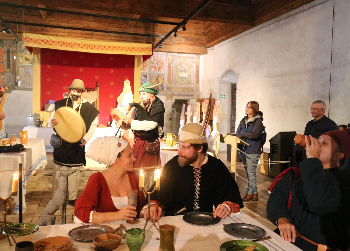Des personnages costumés se régalent autour d'une table, avec plusieurs musiciens en arrière-plan