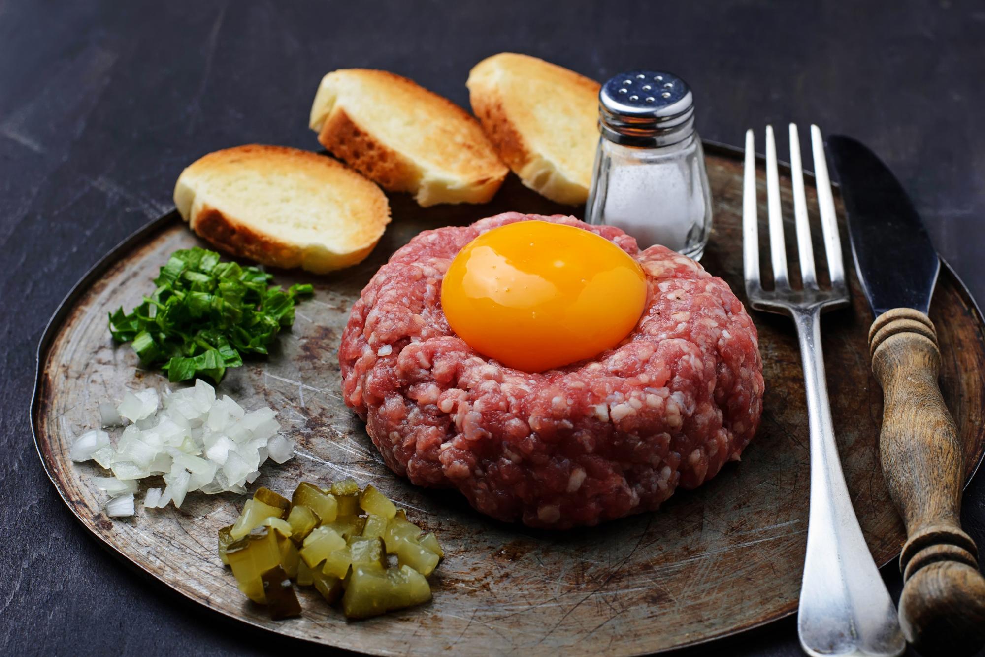 Fresh beef tartar with egg, pickled cucumber and onion. Selective focus