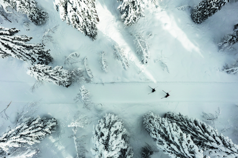 Blick von oben auf eine Frau und ein Mann beim Langlaufen in tief verschneitem Wald.