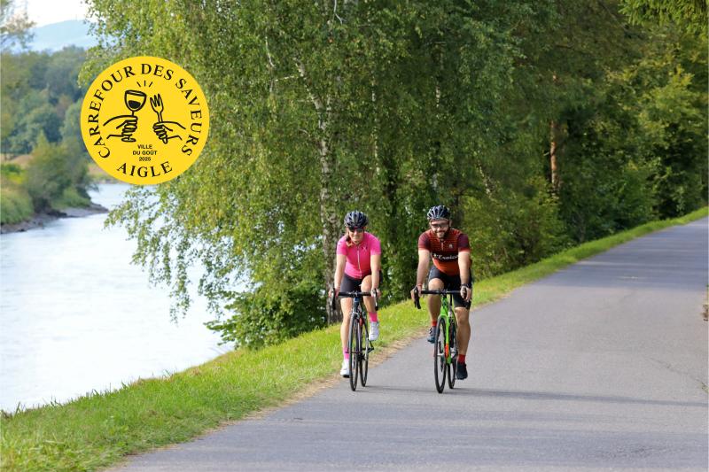 Two people cycling next to the Rhône, with AVDG logo