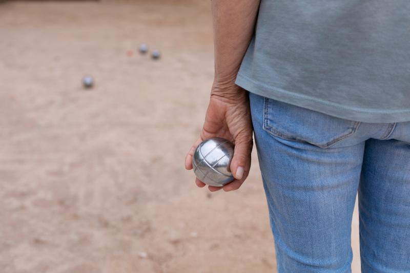 Person with a pétanque ball in their hand in front of the court